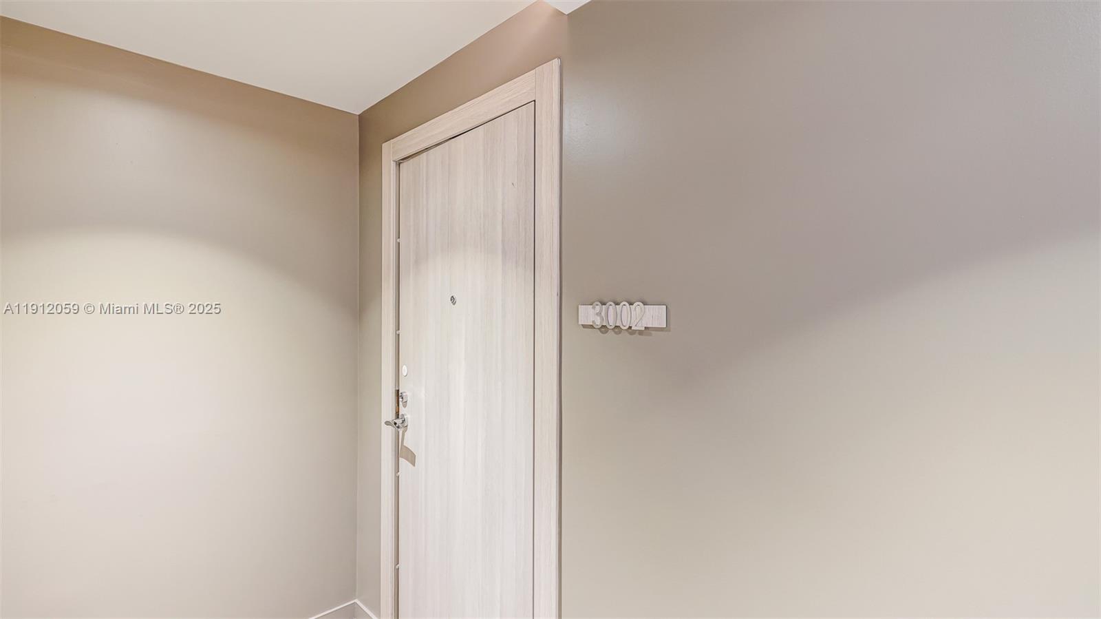 A light-colored wooden door with a room number sign is set in a beige wall — 1000 Brickell Plz # 3002, Miami FL 33131, MIAMI, FL