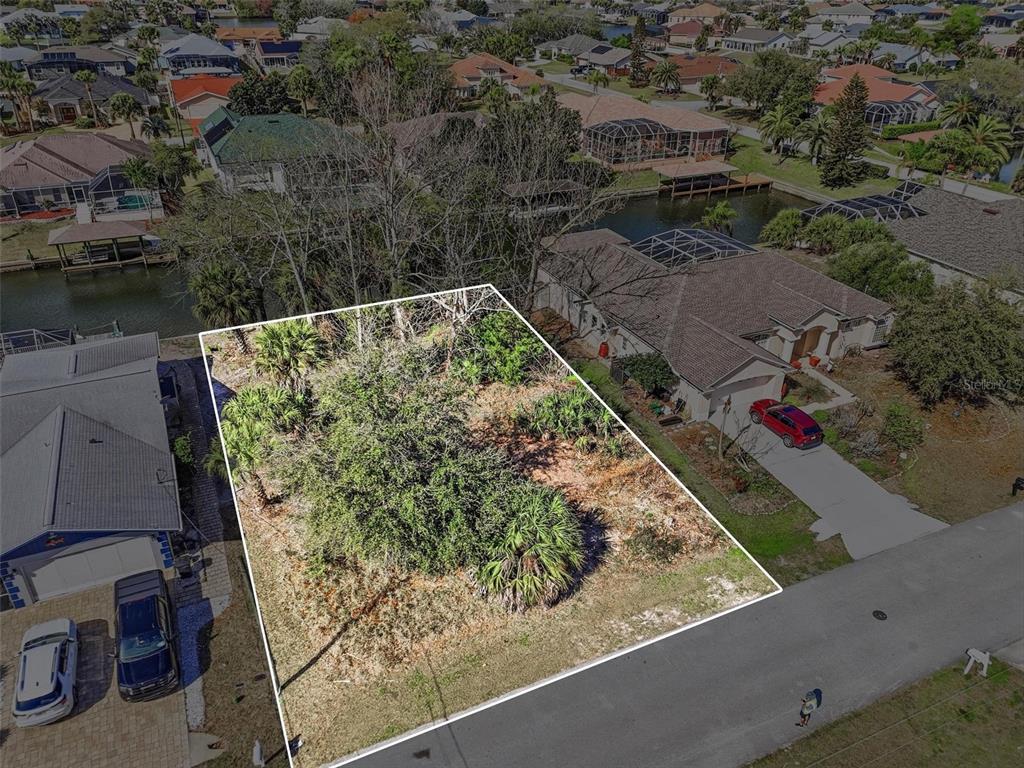 An aerial view shows a vacant, wooded residential lot situated between two houses and water — 35 CORAL REEF COURT N, PALM COAST, FL