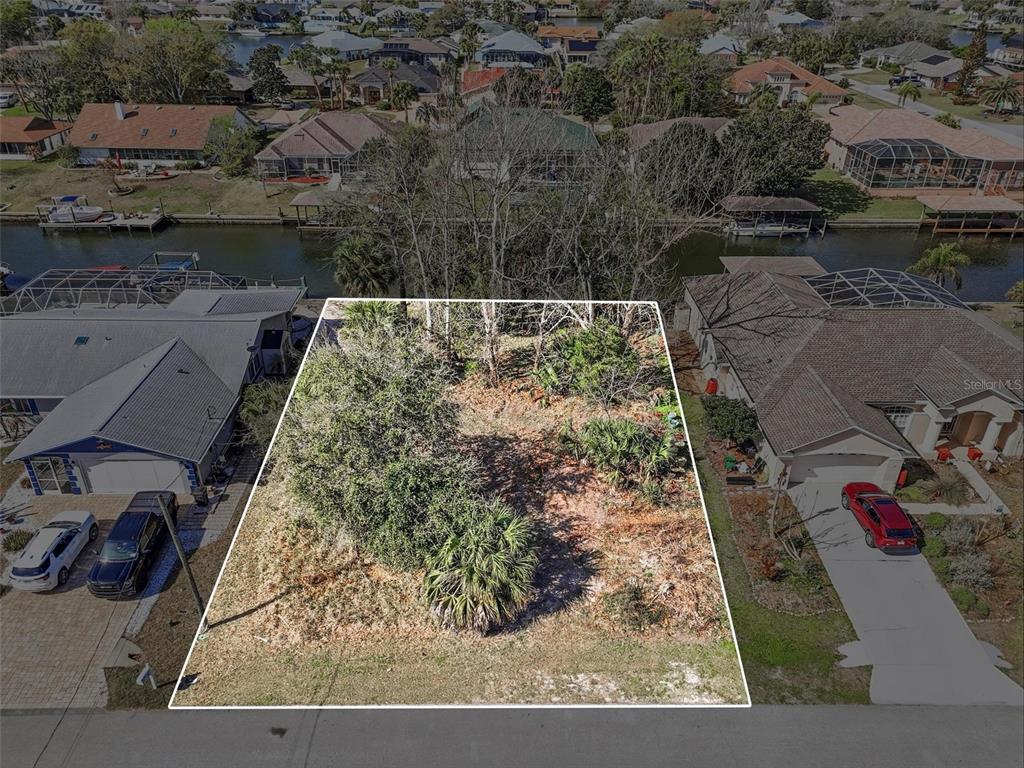 An aerial view shows a vacant, wooded residential lot situated between two houses and waterfront — 35 CORAL REEF COURT N, PALM COAST, FL