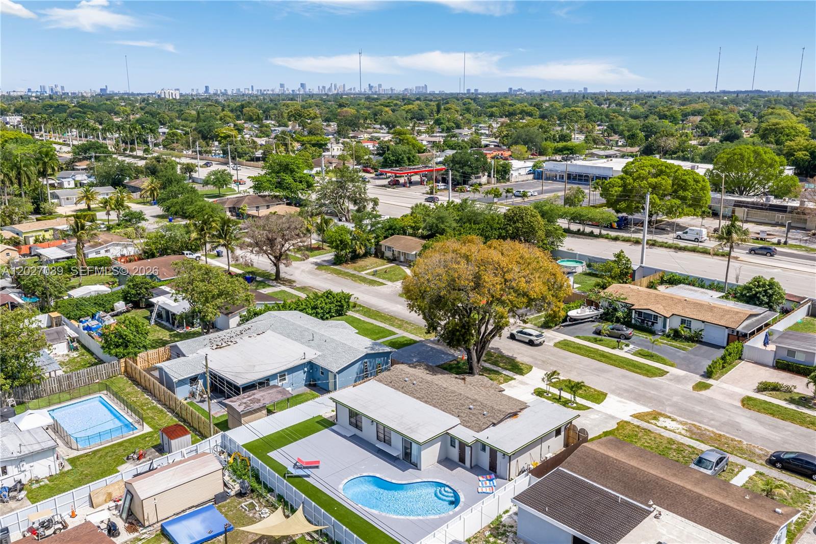 An aerial view shows residential houses with swimming pools and a distant city skyline — 7051 Tyler St, Hollywood FL 33024, HOLLYWOOD, FL