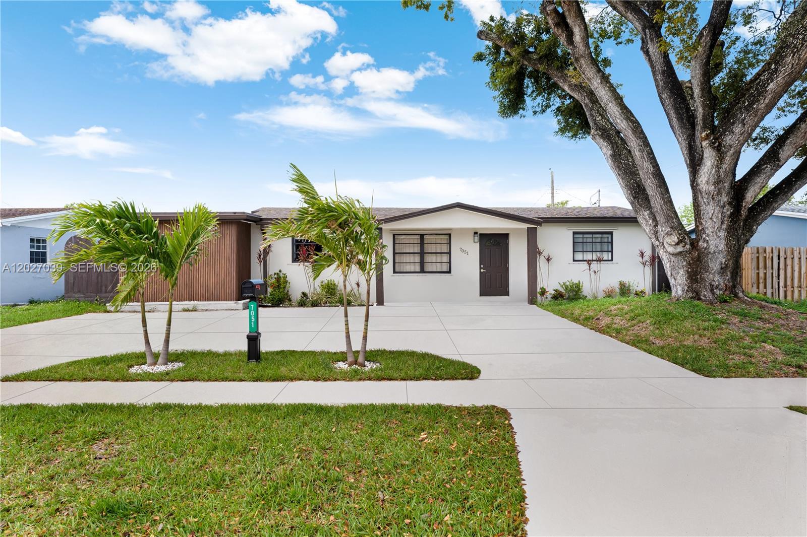 A single-story house with a white exterior, a dark front door, and a large tree — 7051 Tyler St, Hollywood FL 33024, HOLLYWOOD, FL