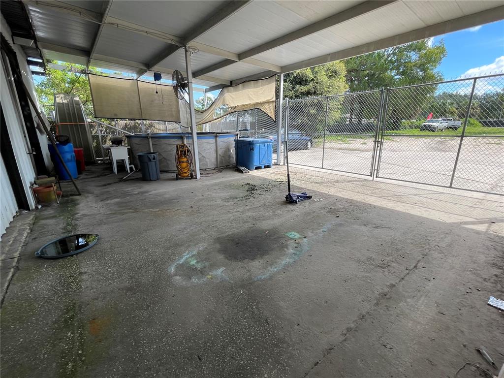A covered concrete patio features a pool, storage containers, a floor jack, and chain-link fencing — 2909 OLD WINTER GARDEN ROAD, ORLANDO, FL