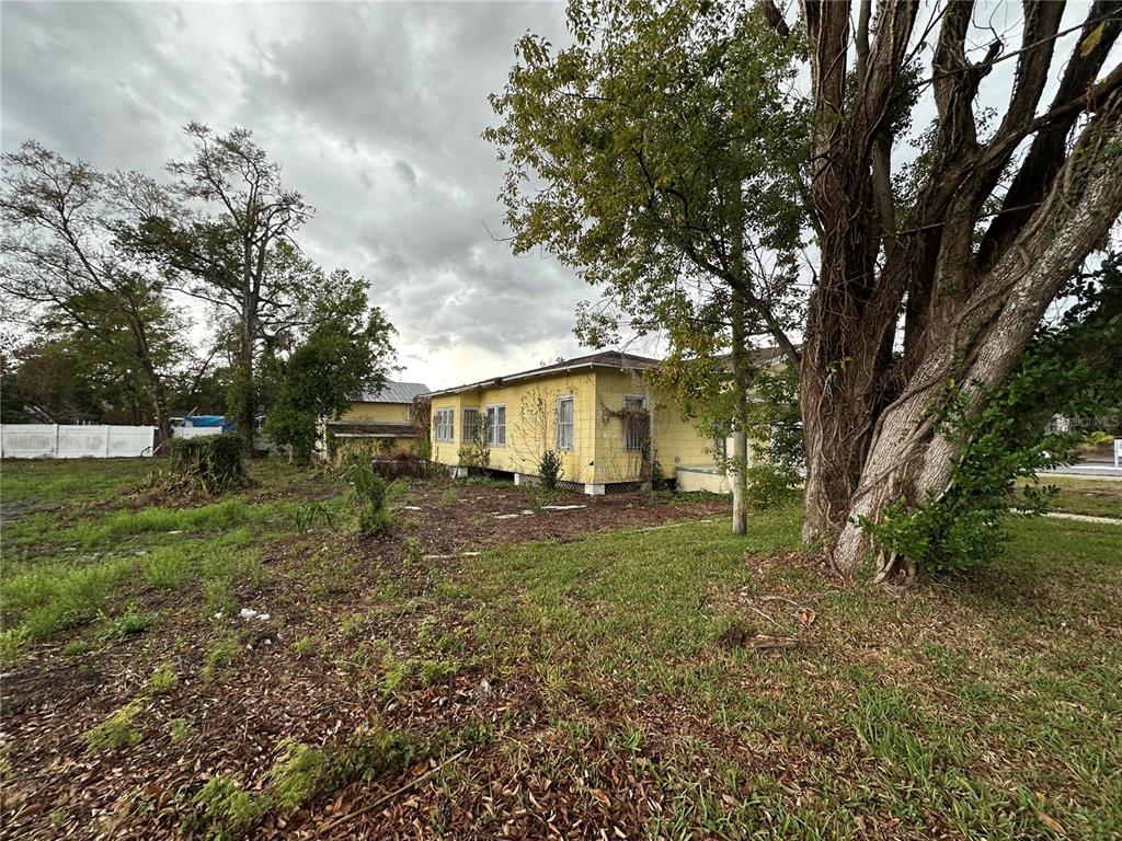A yellow, single-story house with a pier foundation sits on a grassy, tree-filled lot — 3210 N TAMPA STREET, TAMPA, FL