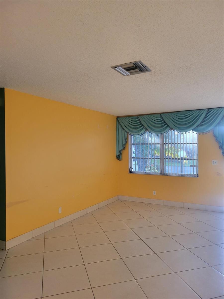 An empty room with yellow walls, light-colored floor tiles, and a window with blue curtains — 1170 NW 90th Avenue, Plantation FL 33322, PLANTATION, FL