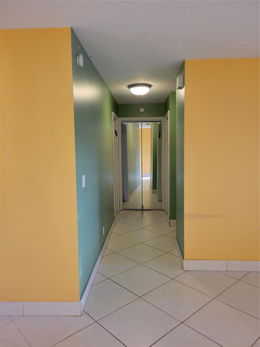 A hallway with yellow and green walls, white tile flooring, and mirrored closet doors — 1170 NW 90th Avenue, Plantation FL 33322, PLANTATION, FL
