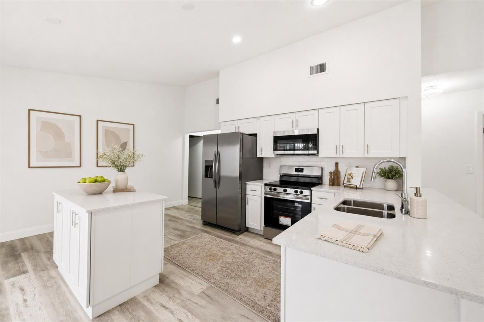 A modern white kitchen features stainless steel appliances, a center island, and light wood flooring — 905 NW 22nd Avenue, Delray Beach FL 33445, DELRAY BEACH, FL