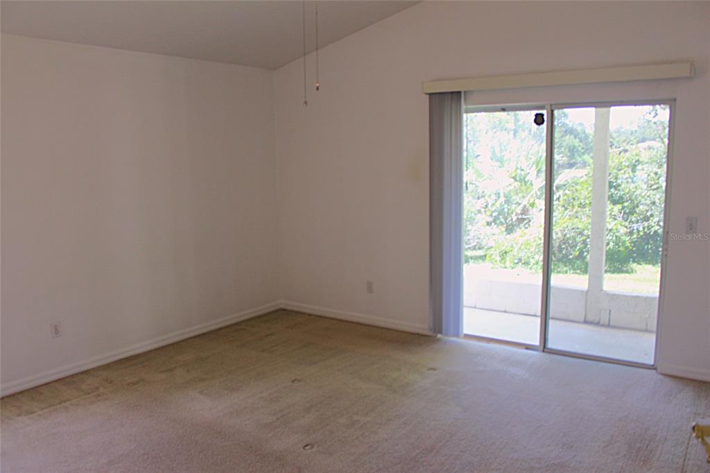 An empty room with beige carpeting, white walls, and a sliding glass door to a patio — 771 MOUNTAIN ASH, DELTONA, FL