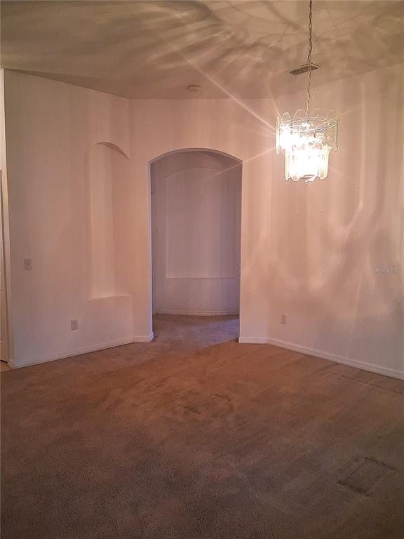 An interior view of a carpeted room featuring an arched entryway and a hanging chandelier — 771 MOUNTAIN ASH, DELTONA, FL