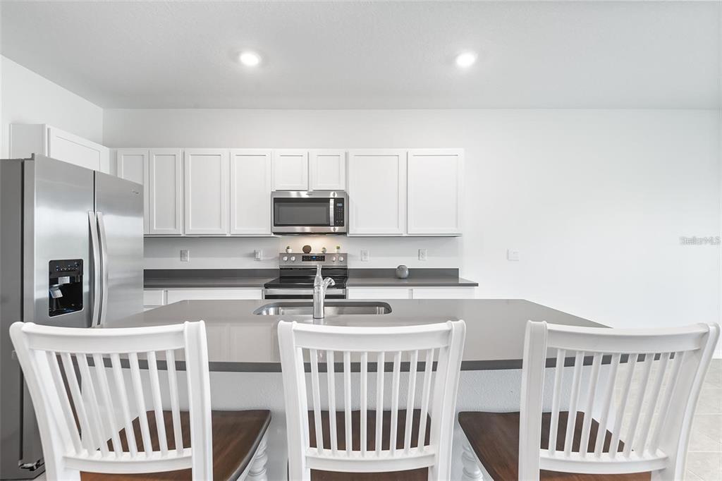A kitchen features white cabinets, stainless steel appliances, a grey countertop, and three white chairs — 11236 CRESCENT DEER DRIVE, LAND O LAKES, FL