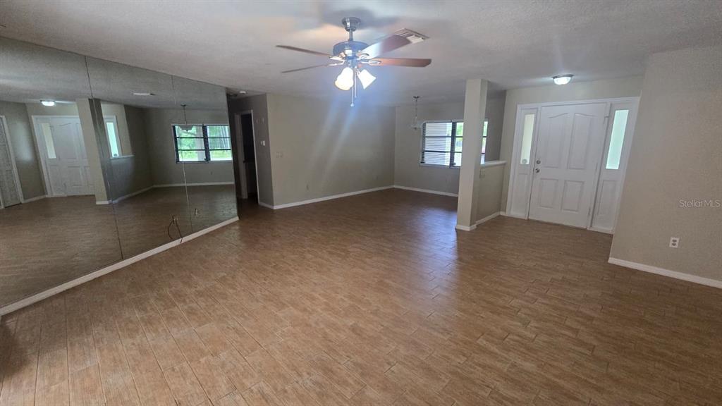A spacious living area features wood-look tile flooring, a ceiling fan, and a mirrored wall — 5461 OAKRIDGE DRIVE, PALM HARBOR, FL