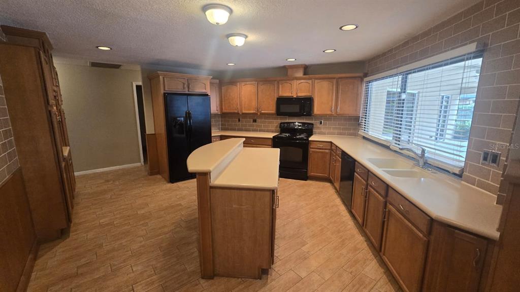 A kitchen features wood cabinets, black appliances, a central island, and light-colored tile flooring — 5461 OAKRIDGE DRIVE, PALM HARBOR, FL