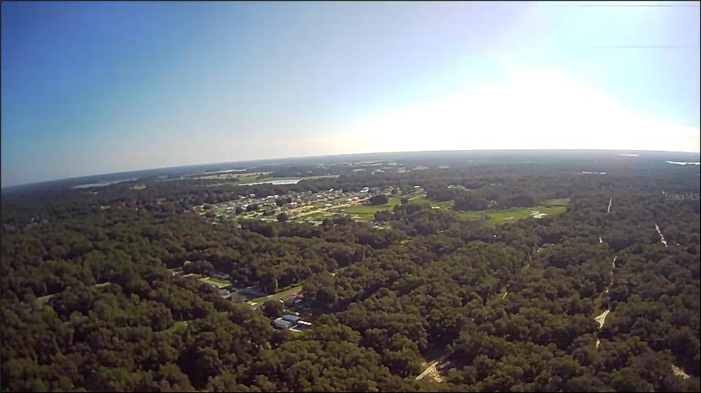 An aerial view shows a residential neighborhood surrounded by dense forest under a bright sky — 1105 CONSTITUTION WAY, INVERNESS, FL
