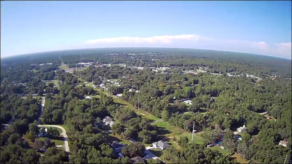 An aerial view shows a residential neighborhood surrounded by dense trees under a clear sky — 1105 CONSTITUTION WAY, INVERNESS, FL