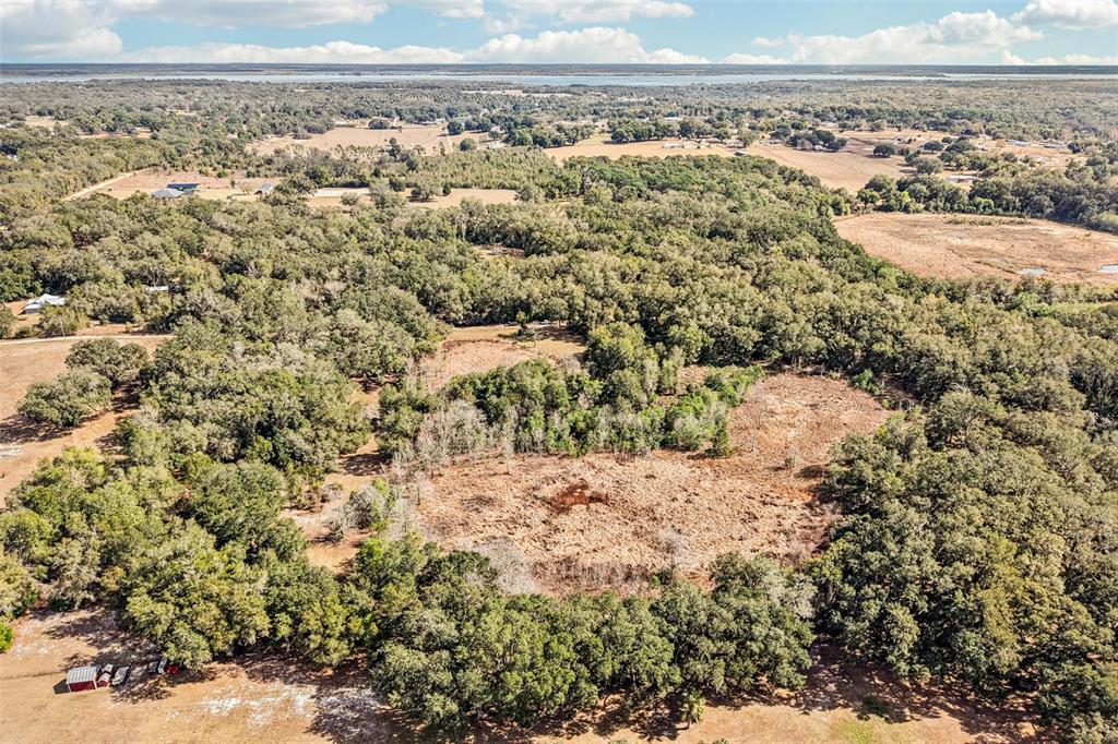 An aerial view shows a large, cleared grassy field surrounded by dense woods and trees — HARRIS LAKE ROAD, LADY LAKE, FL