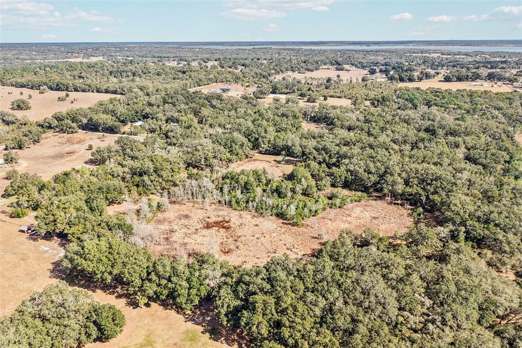 An aerial view shows a large, partially cleared plot of land surrounded by dense trees — HARRIS LAKE ROAD, LADY LAKE, FL