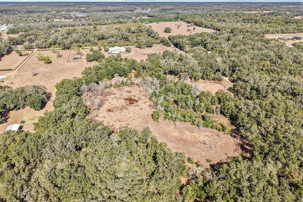 An aerial view shows a large, cleared grassy field surrounded by dense forest — HARRIS LAKE ROAD, LADY LAKE, FL