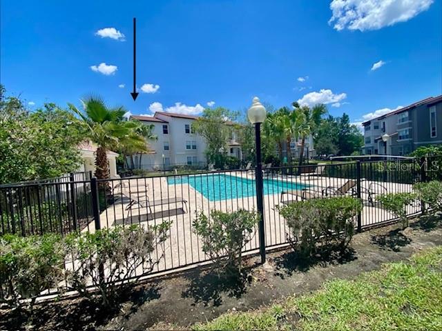 A swimming pool sits in front of a multi-story apartment building under a blue sky — 5144 CONROY ROAD UNIT 38, ORLANDO, FL