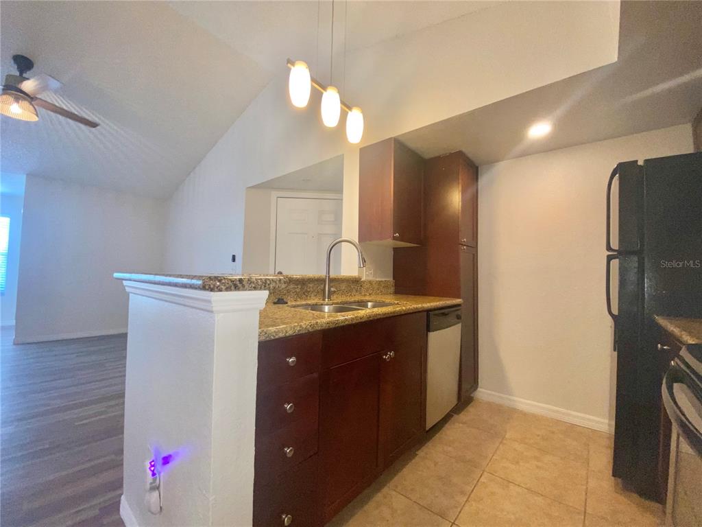 A kitchen features dark wood cabinets, granite countertops, a stainless sink, and a black refrigerator — 5144 CONROY ROAD UNIT 38, ORLANDO, FL