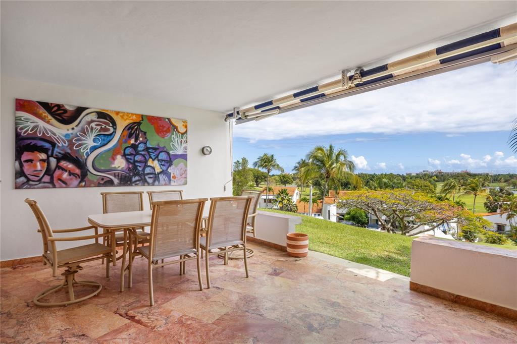 A covered patio features a dining set, colorful wall art, and a view of palm trees — RIO MAR CLUSTER 3, VILLA DEL AMANECER, RIO GRANDE, PR