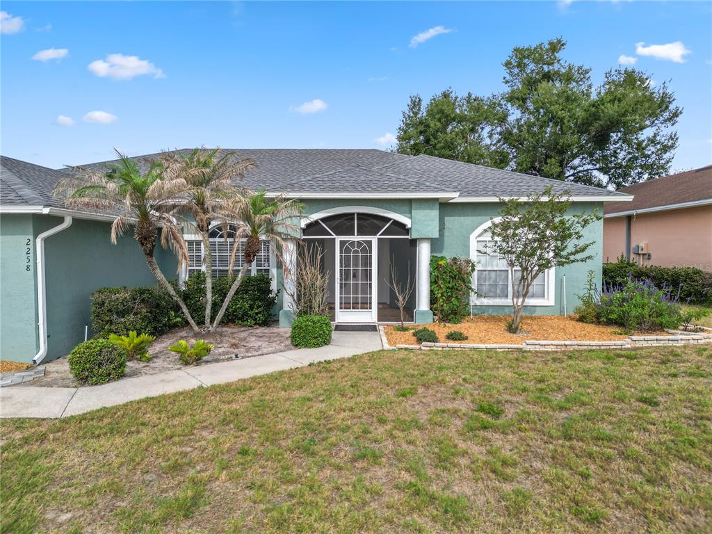 A single-story house with a green stucco exterior, a screened entryway, and a front lawn — 2258 COLONY CLUB DRIVE, LAKELAND, FL