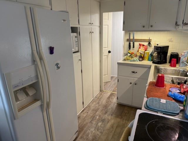 A kitchen features white cabinets, a side-by-side refrigerator, and wood-look flooring — 620 49TH AVENUE W, BRADENTON, FL