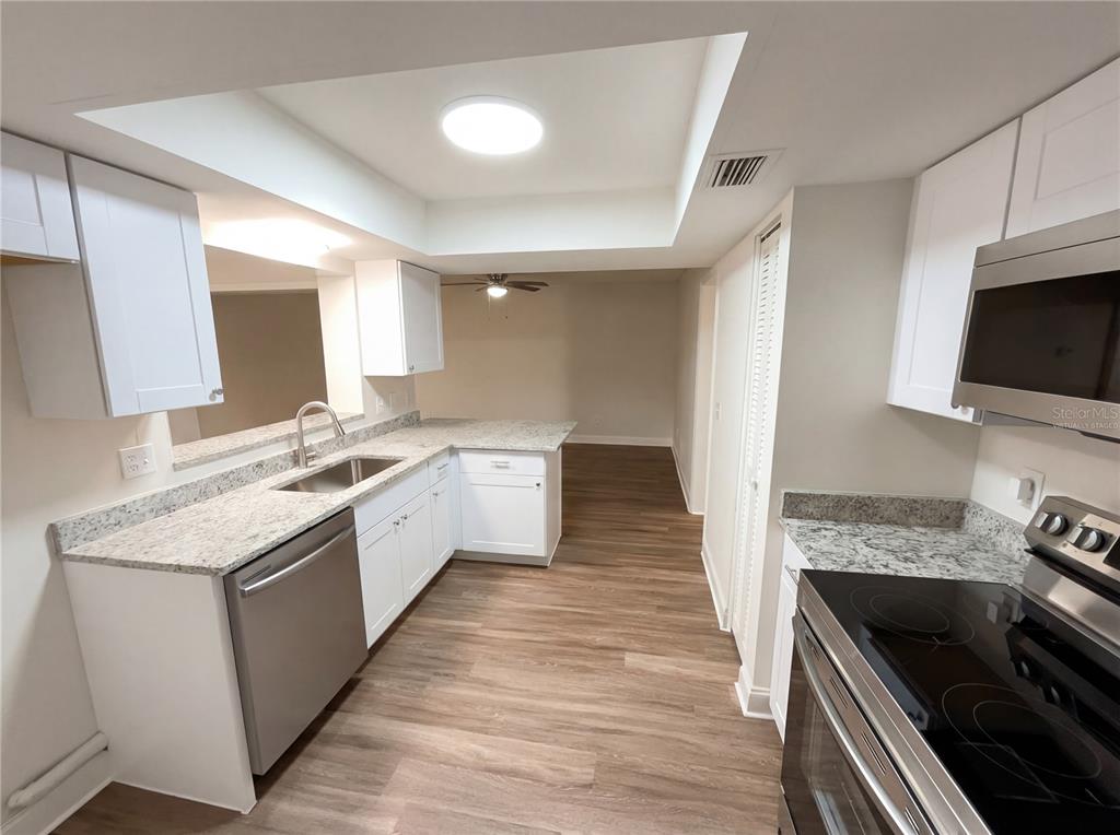 A kitchen with white cabinets, granite countertops, stainless steel appliances, and wood-look flooring — 2052 LEANNE COURT, WINTER PARK, FL