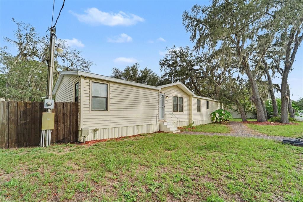 A light-colored mobile home with vinyl siding sits on a grassy lot with large trees — 12464 LANTANA AVENUE, NEW PORT RICHEY, FL