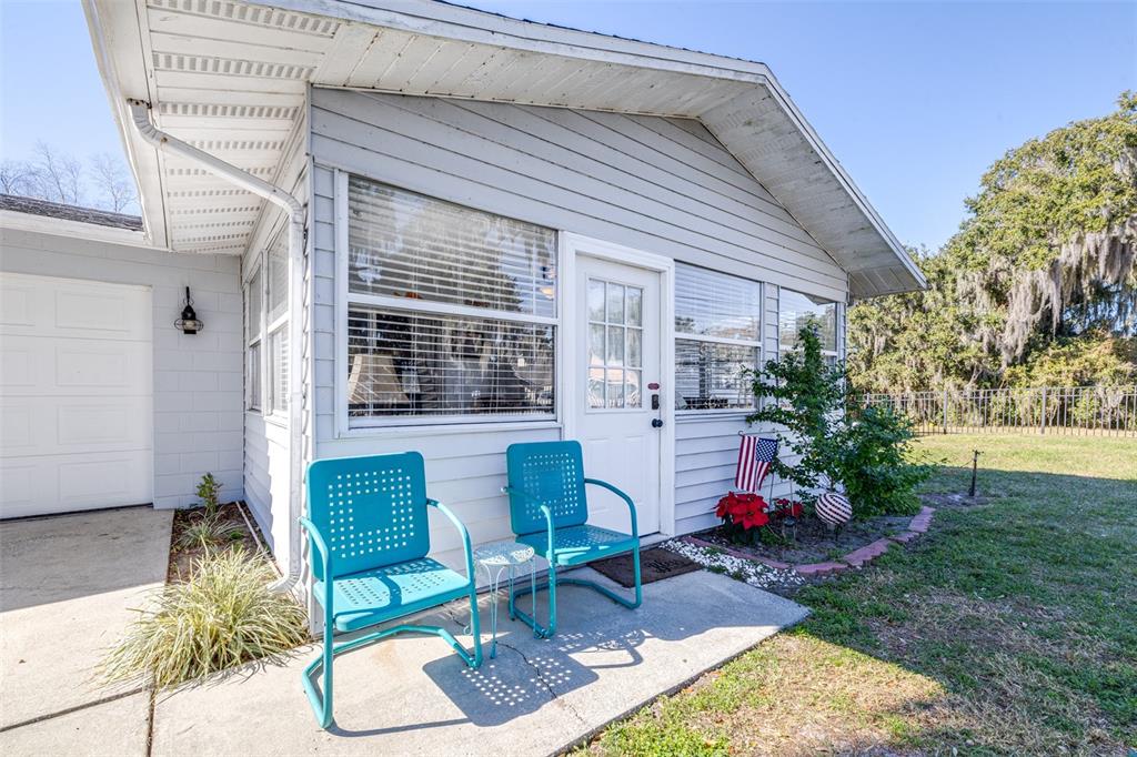 A light gray house exterior features a concrete patio with two bright blue metal chairs — 4742 CYPRESS DRIVE, LAKE WALES, FL