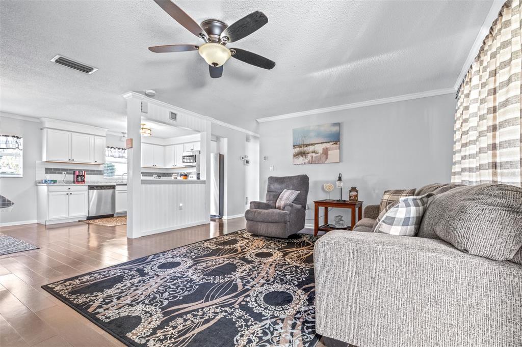 A living room with a patterned rug, gray sofa, recliner, and an adjacent white kitchen — 4742 CYPRESS DRIVE, LAKE WALES, FL