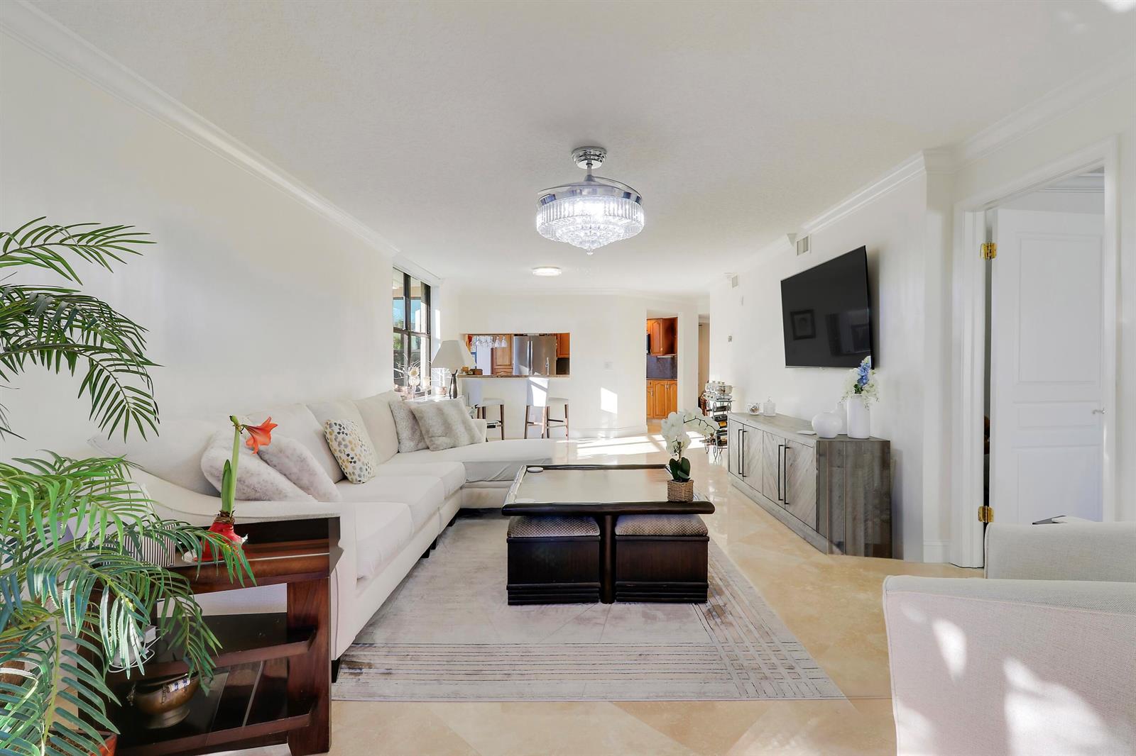 A bright living room features a white sectional sofa, a coffee table, and a television — 235 Bay Colony Drive N, Juno Beach FL 33408, JUNO BEACH, FL