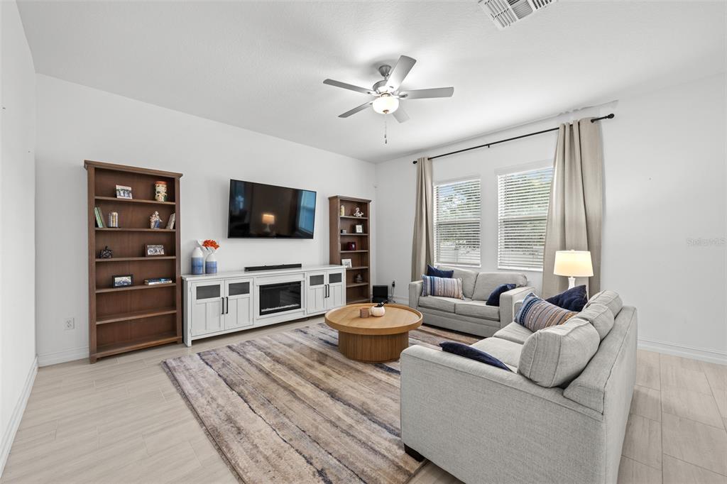 A living room features light tile flooring, two sofas, a television, and wooden bookshelves — 7711 S SWOOPE STREET, TAMPA, FL