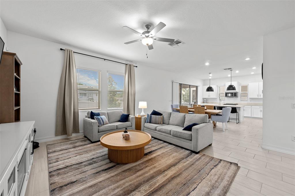 A living room with a gray sofa and loveseat opens to a kitchen with white cabinets — 7711 S SWOOPE STREET, TAMPA, FL
