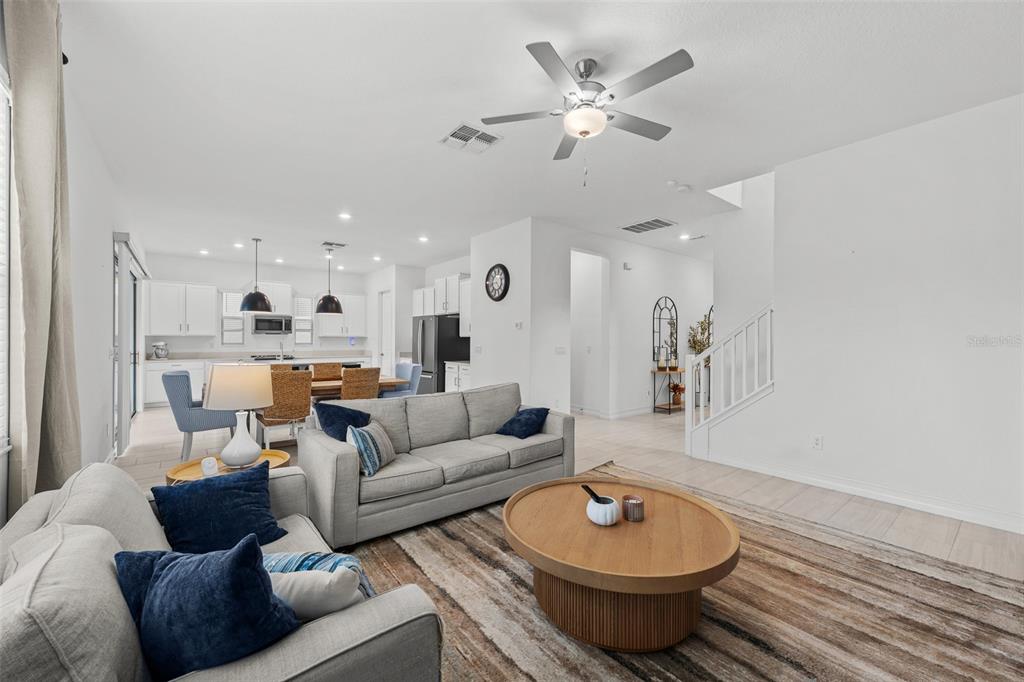 An open-concept living room features a gray sofa, a round wooden coffee table, and a kitchen — 7711 S SWOOPE STREET, TAMPA, FL
