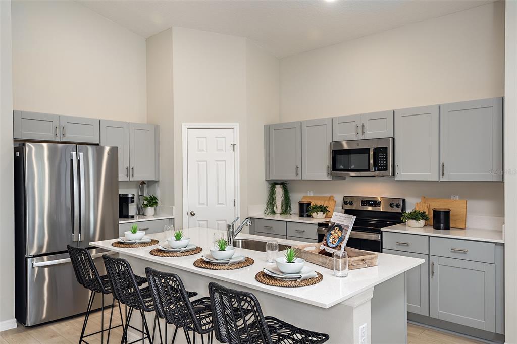 A kitchen features gray cabinets, stainless steel appliances, a white island, and black woven chairs — 34987 ARBOR RETREAT DRIVE, DADE CITY, FL