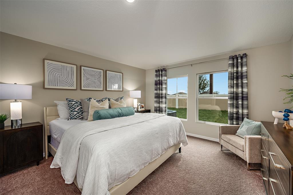A bedroom features a king bed, two nightstands with lamps, and a chair by the window — 34987 ARBOR RETREAT DRIVE, DADE CITY, FL