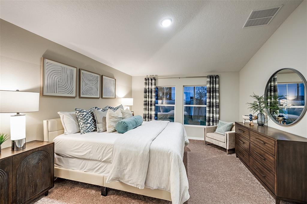A bedroom features a king bed, a wooden dresser with a mirror, and a small armchair — 34987 ARBOR RETREAT DRIVE, DADE CITY, FL