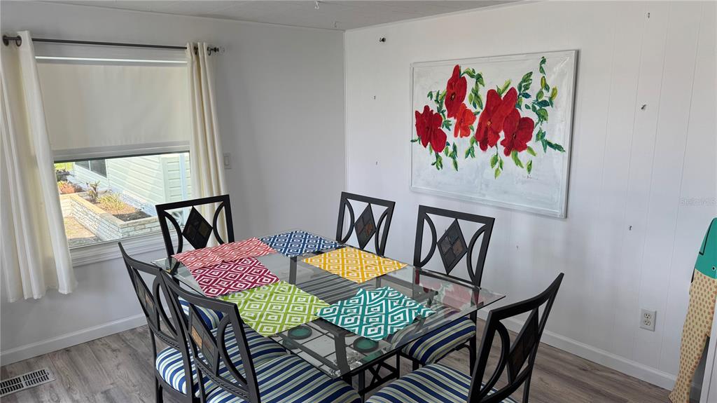 A dining room features a glass-top table with patterned placemats, six chairs, and floral wall art — 1704 PENNSYLVANIA AVENUE, BRADENTON, FL