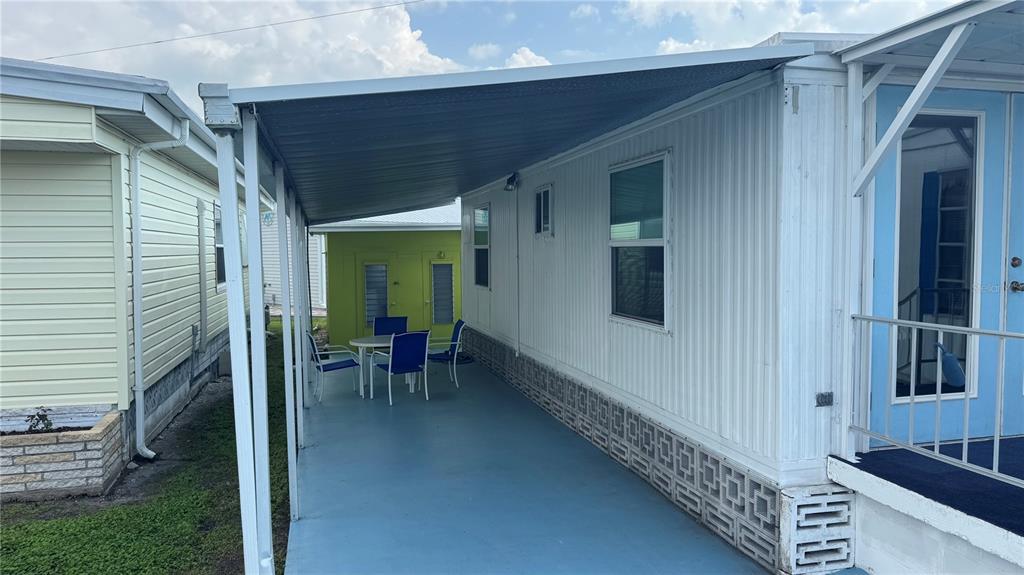 A covered carport area with a concrete floor sits beside a white mobile home — 1704 PENNSYLVANIA AVENUE, BRADENTON, FL