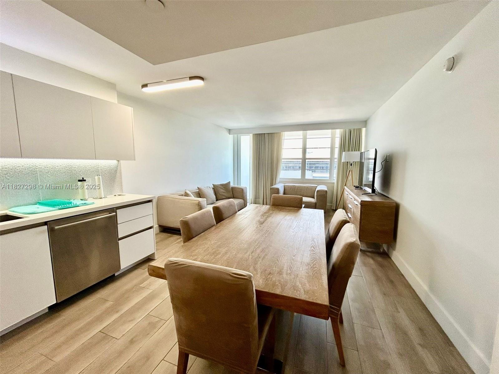 A dining area with a wooden table and chairs sits adjacent to a modern kitchen — 100 Lincoln Rd # 1429, Miami Beach FL 33139, MIAMI BEACH, FL