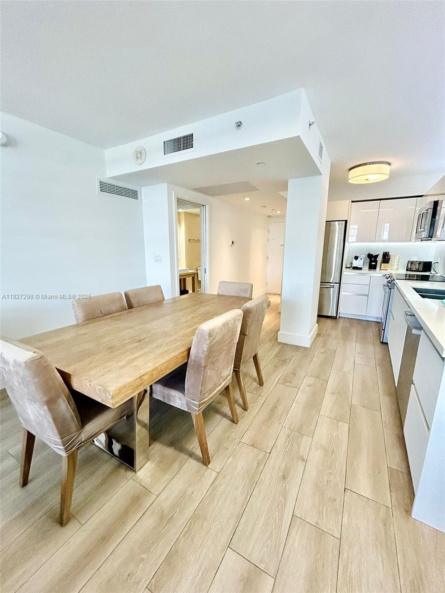 A dining area with a wooden table and chairs sits adjacent to a modern kitchen — 100 Lincoln Rd # 1429, Miami Beach FL 33139, MIAMI BEACH, FL