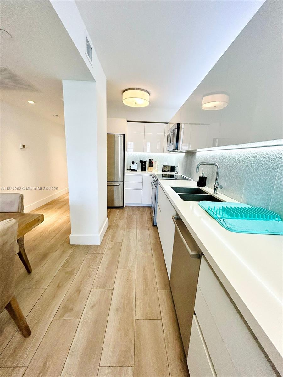 A modern kitchen features white cabinetry, stainless steel appliances, and light wood-look flooring — 100 Lincoln Rd # 1429, Miami Beach FL 33139, MIAMI BEACH, FL