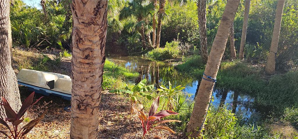 A small boat sits on the bank of a narrow, tree-lined canal in a backyard — 6394 MCKINLEY TERRACE, ENGLEWOOD, FL