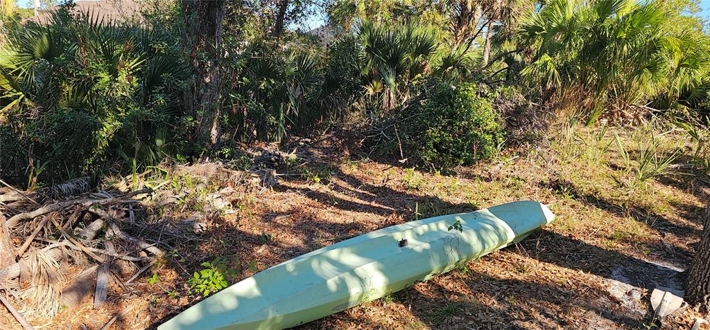 A light green kayak rests on the ground in a wooded, natural outdoor area — 6394 MCKINLEY TERRACE, ENGLEWOOD, FL