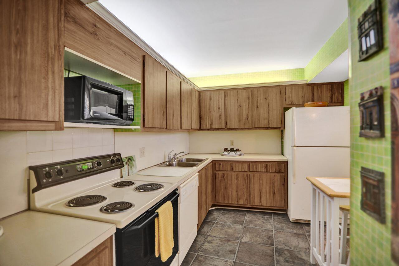 A kitchen features wood-grain cabinets, a white stove, a white refrigerator, and green tiled walls — 100 Ocean Trail Way # 109, Jupiter FL 33477, JUPITER, FL
