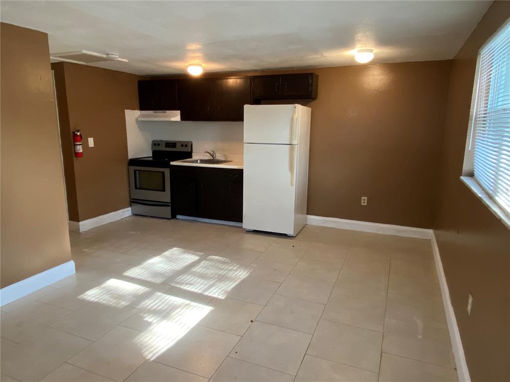 A kitchen with brown walls, dark cabinets, a white refrigerator, and light-colored tile flooring — 1609 E 143RD AVENUE UNIT 105-108, TAMPA, FL