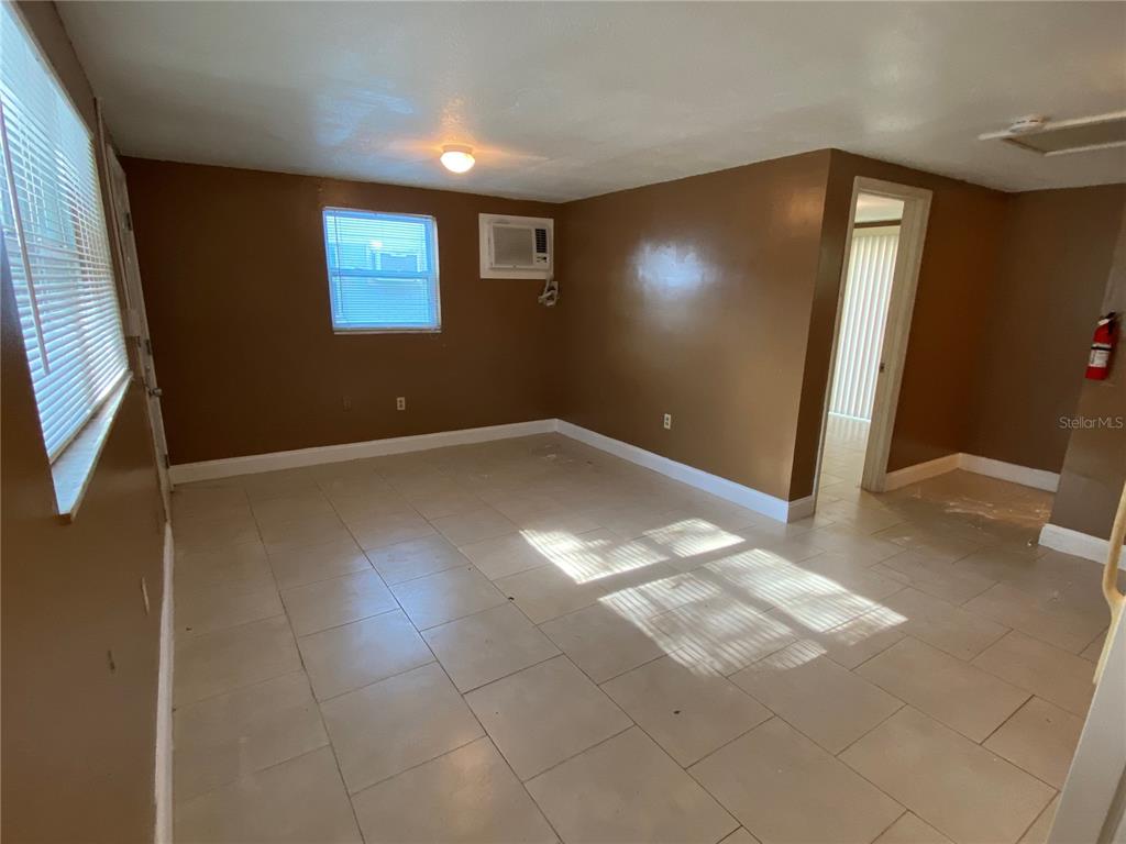 An empty room with brown walls, light-colored tile flooring, a window, and an air conditioner — 1609 E 143RD AVENUE UNIT 105-108, TAMPA, FL