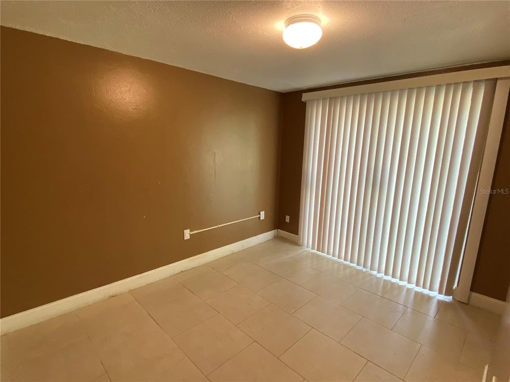 An empty room features tan walls, light-colored tile flooring, and vertical blinds over sliding doors — 1609 E 143RD AVENUE UNIT 105-108, TAMPA, FL
