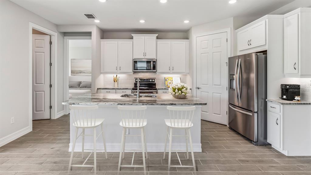 A kitchen features white cabinets, a marble-topped island with three stools, and stainless steel appliances — 12769 SEAGRASS DRIVE, PUNTA GORDA, FL