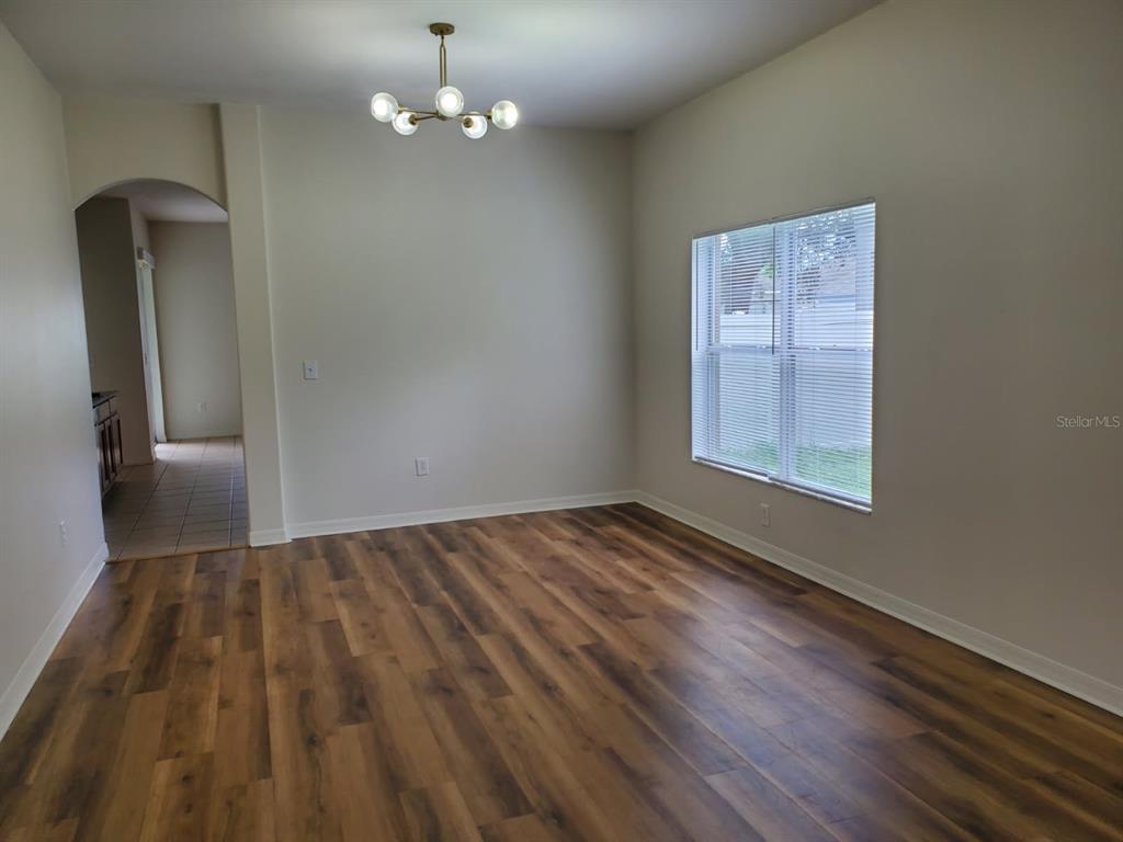 An empty dining room features wood-look flooring, a modern chandelier, and a window with blinds — 12148 LUFTBURROW LANE, HUDSON, FL