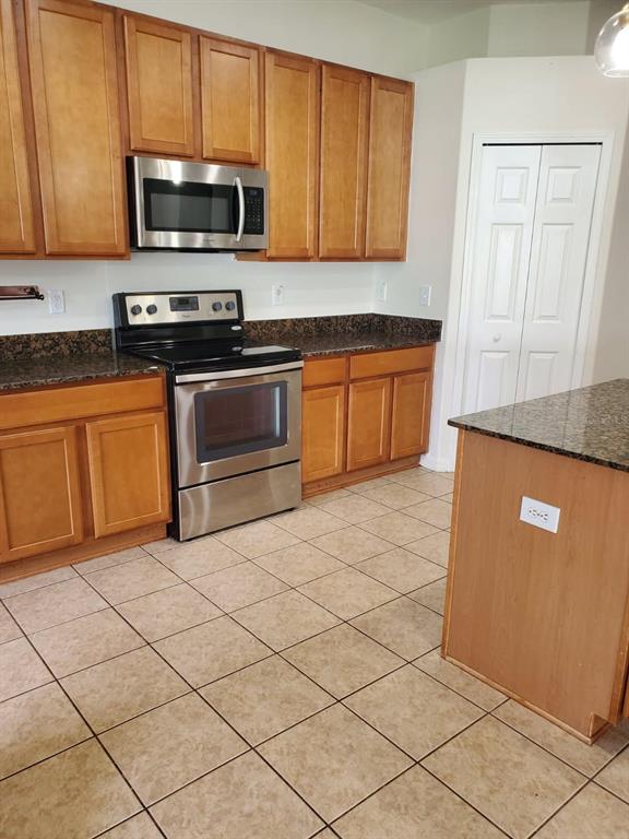 A kitchen features wood cabinets, stainless steel appliances, dark granite countertops, and tiled flooring — 12148 LUFTBURROW LANE, HUDSON, FL